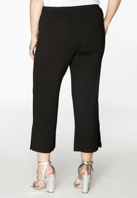 Schwarze cropped Hosen aus glattem Stoff. Verfügt über ein gerades Bein-Design und seitliche Schlitze am Saum. Kombiniert mit metallic Blockabsatzsandalen.