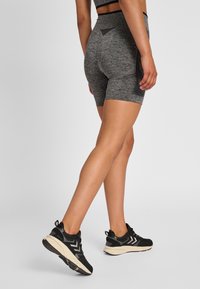 Pantaloni sportivi grigi con un design aderente, realizzati in tessuto testurizzato, dotati di una tasca laterale. Sneakers nere completano l'outfit.