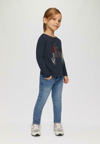 Marineblaue Langarmshirt mit einem Pailletten-Rentierdesign, kombiniert mit blauen Jeans und mehrfarbigen Sneakers. Einfaches, lässiges Outfit.