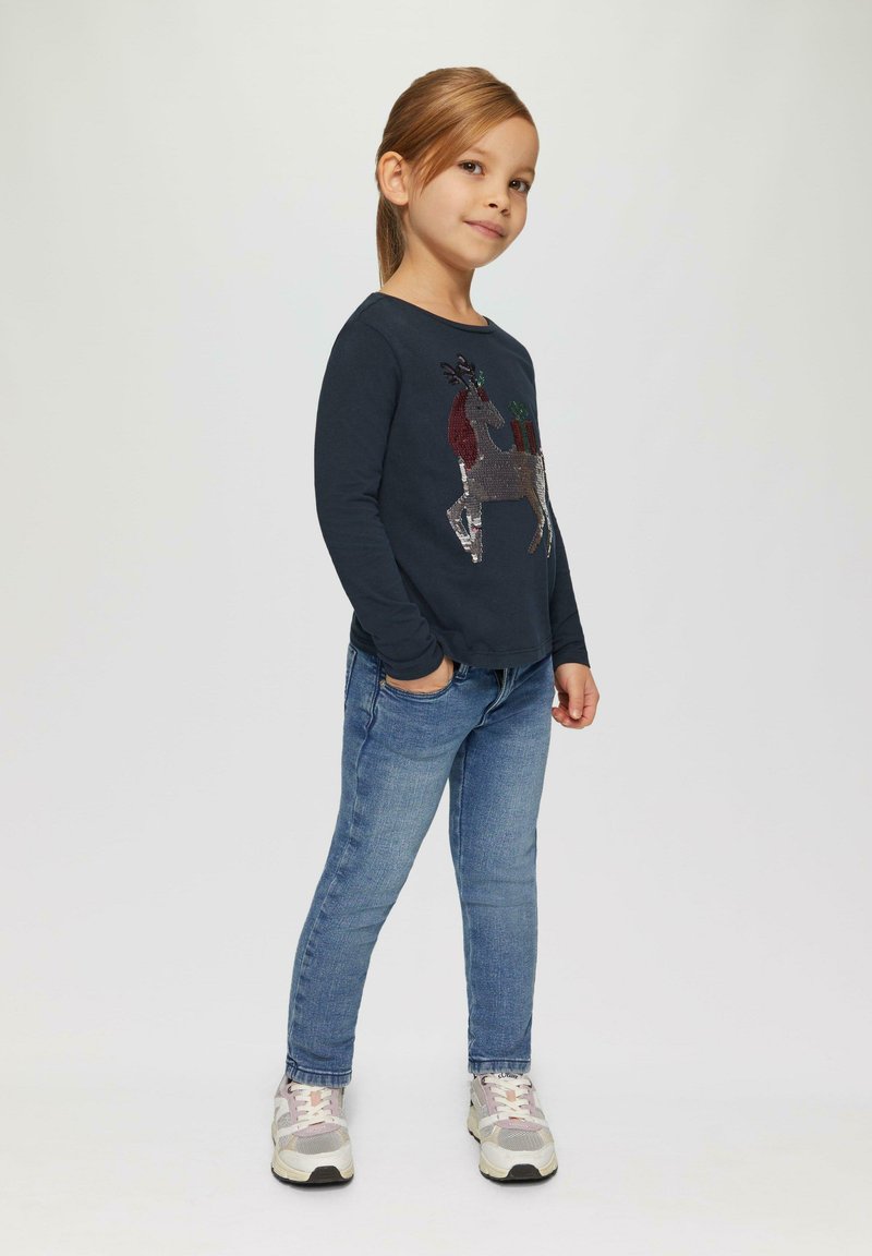 Marineblaue Langarmshirt mit einem Pailletten-Rentierdesign, kombiniert mit blauen Jeans und mehrfarbigen Sneakers. Einfaches, lässiges Outfit.