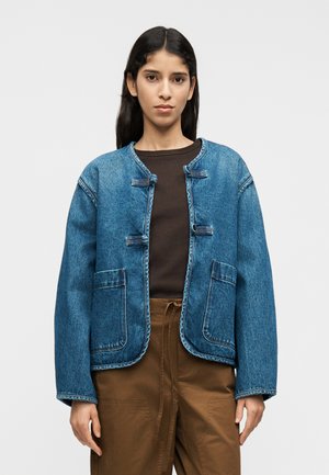 Veste en denim de couleur bleu vif, avec un col rond, des poches avant et des fermetures à bascule. Le design présente une coupe ample et des coutures visibles.