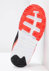 Svart sneakersula med texturerat mönster, med orange detalj och vit mellansula. Noterbara spår förbättrar grepp och flexibilitet.