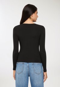 Czarny top z długim rękawem i okrągłym dekoltem, wykonany z gładkiego materiału. Tył jest dopasowany, a model nosi jasnoniebieskie jeansy z wysokim stanem.