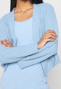 Cardigan azzurro chiaro con texture e vestibilità comoda. Maniche lunghe, apertura frontale e dettaglio a coste lungo i bordi. Abbinabile a un top coordinato.