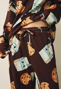 Brown ribbed loungewear set featuring playful milk and cookie prints. The fabric has a soft texture, with an elastic waistband and drawstring.