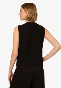 Zwarte mouwloze top van gestructureerde stof. Ronde halslijn en rugdetail, zoom valt op de taille. Gecombineerd met donkere onderkleding.