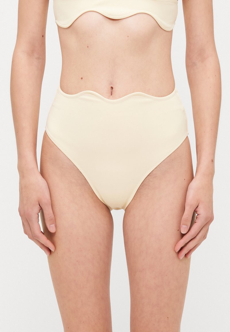Hohe Bikini-Hosen aus weichem, blassgelbem Stoff mit einem Wellenmuster am Bund, die über glatte Nähte und eine figurbetonte Form verfügen.