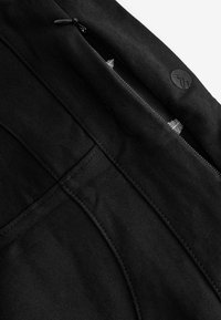 Pantalons noirs avec une poche zippée, fabriqués à partir d'un tissu texturé. Caractéristiques de coutures subtiles et d'un logo rond sur la taille.