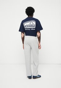 Marineblå t-skjorte med hvitt logo og tekst på baksiden, kombinert med lysegrå joggebukser og blå sko med svart og hvitt striper.