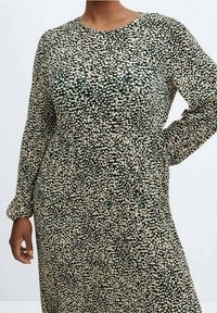 Robe à manches longues de couleur vert foncé avec un motif crémeux à taches. Présente un col rond et un tissu doux avec une silhouette fluide.