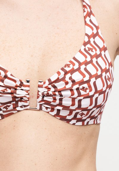 Κοντινό πλάνο ενός μπικίνι με σχέδια από καφέ και λευκά γεωμετρικά σχήματα, που φοριέται σε ανοιχτόχρωμο δέρμα με φακίδες.