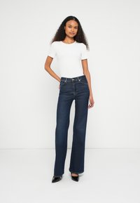 Jean évasé taille haute en denim foncé avec un design classique à cinq poches, associé à un t-shirt blanc ajusté. Talons noirs pointus.