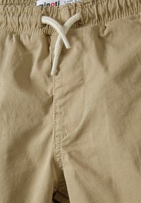 Pantaloni corti beige con cintura elasticizzata e cordoncino, caratterizzati da una texture liscia e dettagli nelle cuciture laterali.