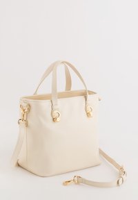 Beige faux leather handbag with two top handles and a removable shoulder strap. Features gold-tone hardware and a structured shape.