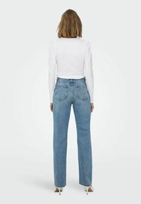 Witte blouse met lange mouwen en opbollende schouders, gecombineerd met lichtblauwe rechtlopende jeans met een klassieke vijf-pocket ontwerp en een lichte wassing.