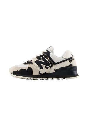 Bielo-čierny tenisky New Balance s potlačou kravy, sieťovinový zvršok, čierna podrážka a veľké logo "N" na boku.