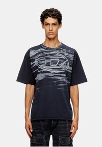 T-shirt bleu marine en tissu doux, arborant un motif de vagues gris contrastant et un logo ovale bien visible sur le devant. Manches courtes.