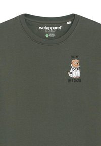 Donkergroene katoenen t-shirt met een cartoon hond in een labjas en de tekst "VERTRAAG ME, IK BEN EEN HOND-DOKTER" ernaast gedrukt.