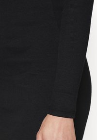 Tissu noir côtelé d'un haut à manches longues, avec une coupe ajustée, une texture subtile et des finitions au niveau des poignets.