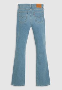 Jeans bleu clair taille haute avec poches arrière, jambes évasées, patch de marque en cuir et étiquette rouge sur la poche droite.