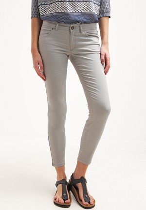 Jeans ajustados de color gris claro con una textura suave y un diseño de cintura media, combinados con sandalias de tiras negras con suela de corcho.
