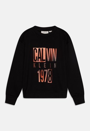 Musta pitkähihainen collegepaita, jossa edessä suuret kuparinväriset kirjaimet "CALVIN KLEIN 1978".