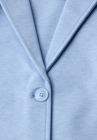 Blazer bleu clair avec un bouton unique fermé sous le revers cranté, mettant en valeur le tissu texturé et les détails de couture.