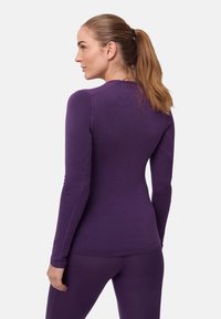 Violetti pitkähihaine paita, jossa on pyöreä kaula-aukko, tiukka malli ja sileä materiaali, yhdistettynä yhdisteisiin legginsseihin.