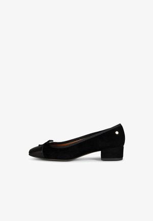 Zapato tipo bailarina de ante negro con tacón bajo, pequeño lazo en la punta y detalle metálico redondo cerca del talón.