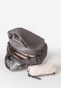 Grijze leren handtas met open ritssluiting en een beige patroonhoes met zwarte ritssluiting op een witte ondergrond.