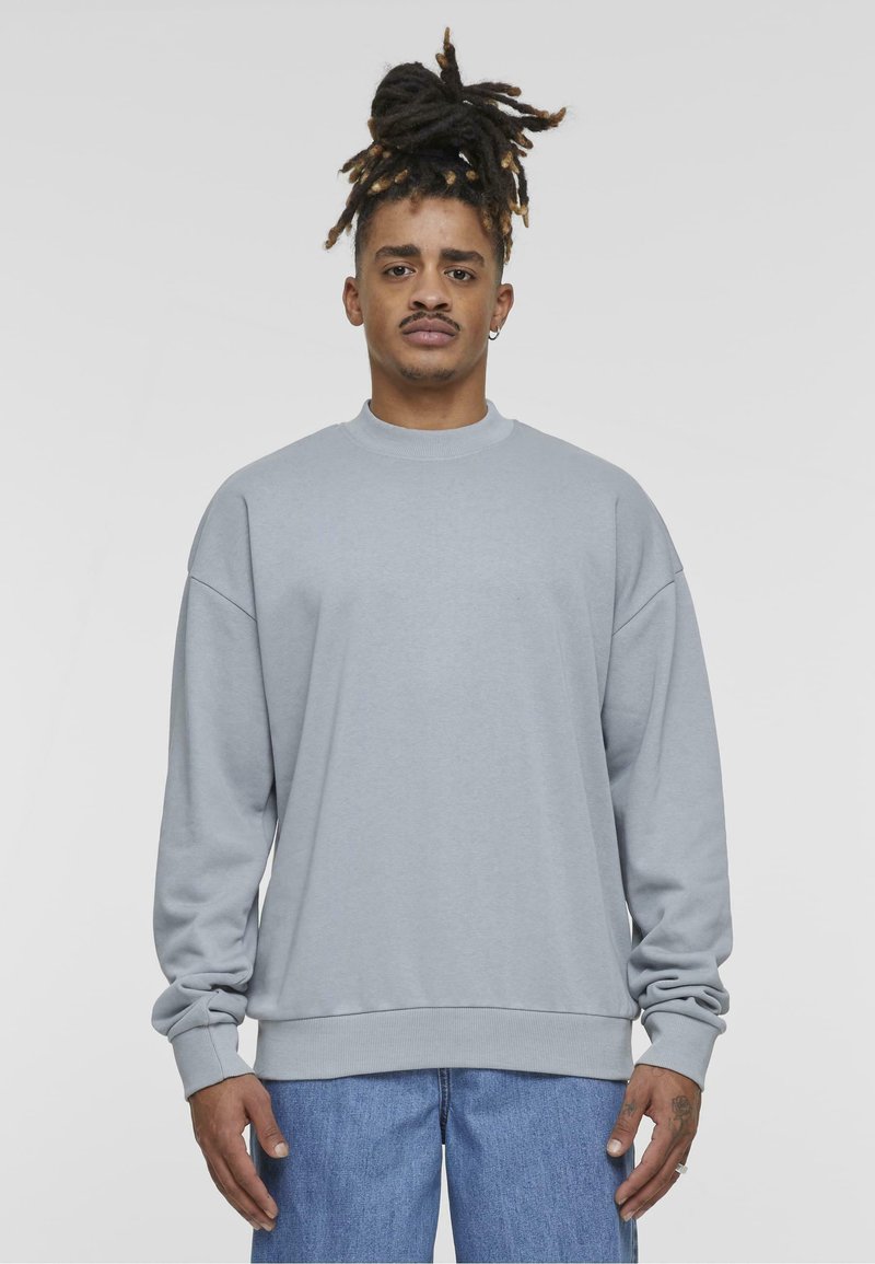 Gråhet genser med rund hals og droppede skuldre, med ribbestrikkede mansjetter og kant. Sammen med blå denimjeans.
