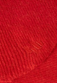 Rode gebreide stof met zichtbare textuur, voorzien van een subtiele geborduurde logo. Het materiaal oogt zacht en licht pluizig.