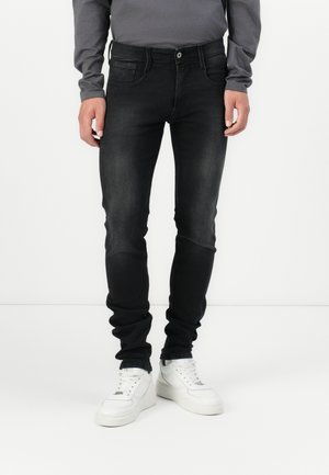 Black skinny jeans with a slight fade, five-pocket design, and a button closure, paired with white high-top sneakers.