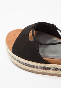 Sandale espadrille noire à bout ouvert avec semelle en jute tressée et perles décoratives argentées, dotée d'une large bride en suède et d'un détail élastique à la cheville.