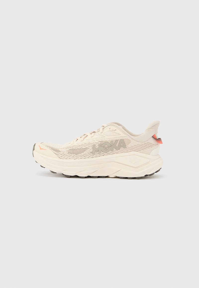 Lys beige løpesko med et teksturert mesh-overside, fremtredende logo, polstret krage og en tykk, forhøyet såle med svart grep.