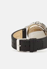Correa de reloj de cuero negro con hebilla de acero inoxidable, con una textura suave y costuras en contraste, vista de lado.