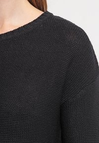 Černý pletený svetr s kulatým výstřihem, zdobený texturovaným vzorem a žebrovaným lemem. Látka působí měkce a lehce.