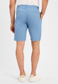 Helle blaue Shorts mit einer glatten Textur, zwei Gesäßtaschen und einem Standardbund. Getragen mit weißen Sneakern und einem schlichten Oberteil.