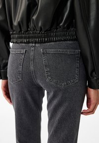 Giacca di pelle nera con vita arricciata, abbinata a jeans in denim grigio scuro con due tasche posteriori e una texture sbiadita.