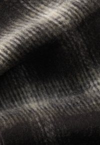 Tessuto di lana texturato nelle tonalità di nero, grigio e crema. Presenta una superficie morbida e pelosa con un motivo di strisce chiare e scure alternate.
