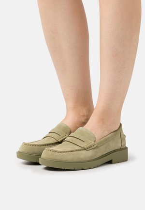 Mocassini in suede verde con una suola bassa e resistente, caratterizzati da dettagli cuciti e una fascia frontale. Il design è semplice e arrotondato, adatto per un abbigliamento casual.