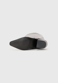 Semelle en caoutchouc noire avec grip texturé ; tige grise lisse avec un design ajusté ; bout pointu et talon carré. Surface plate en dessous pour la stabilité.