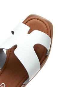 Sandale blanche à brides croisées avec un semelle en cuir marron et une surface lisse. Dotée de bords arrondis et d'un subtil accent cousu.