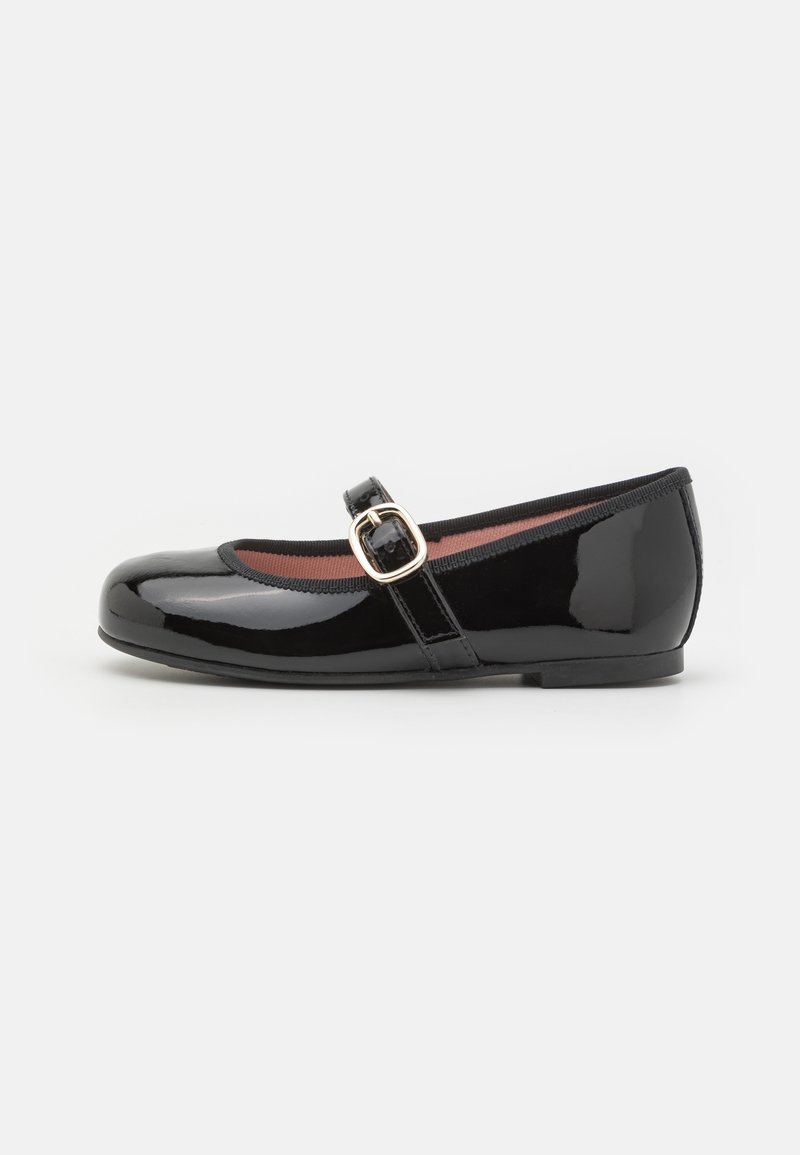 Chaussure Mary Jane en cuir verni noir, bout arrondi, talon plat bas et bride avec boucle dorée sur fond blanc.