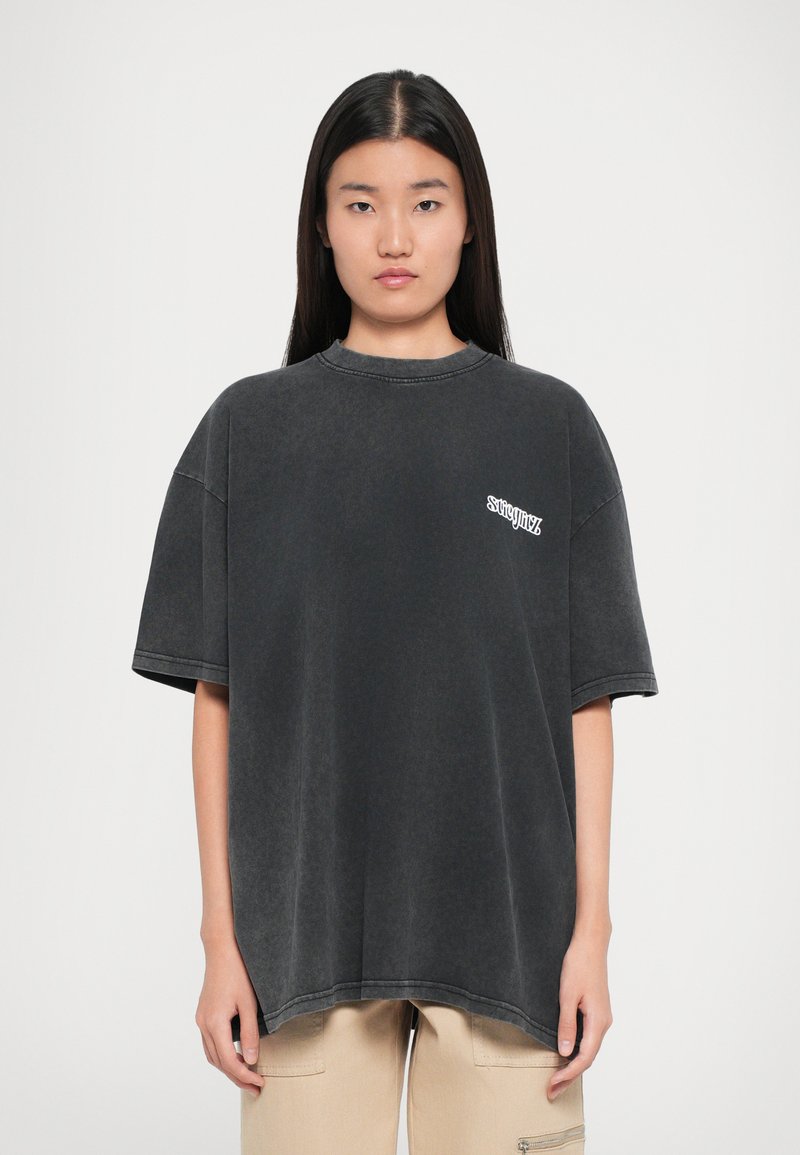 Per didelė juoda T-shirt marškinėliai su išblukusiu paviršiumi, apvaliu kaklu ir trumpomis rankovėmis. Kairėje pusėje yra mažas baltas logotipas.