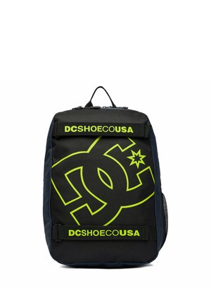 Sac à dos noir avec grand logo DC vert néon et texte "DCSHOECOUSA" sur deux sangles horizontales à l'avant.