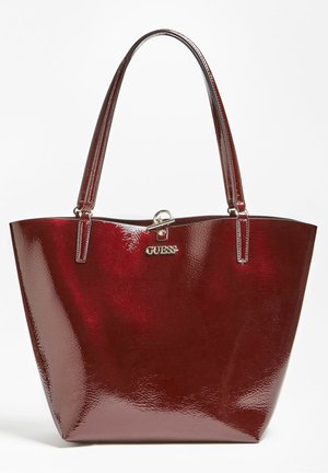 Sac fourre-tout en cuir verni rouge foncé brillant avec deux poignées et logo Guess argenté ainsi que fermoir au centre à l'avant.