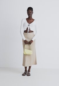 Valkoinen ribattu lyhyt toppi, jossa on solmittava etuosa, beige midi-hame ja keltainen olkalaukku. Mallilla on päällä hopeiset remmisandaalit.