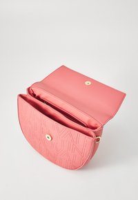 Pink leather crossbody bag with embossed logo, round shape, gold hardware, and a zippered interior pocket. Magnetic snap closure.