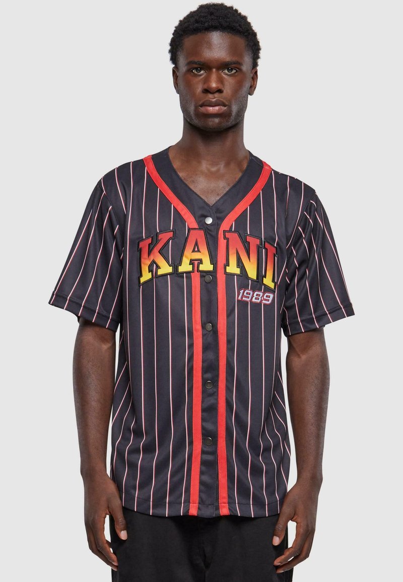 Kortermet, svartstripet jersey med røde detaljer. Har ordet "KANI" i gult og "1989" i rødt. Knappelukking foran.
